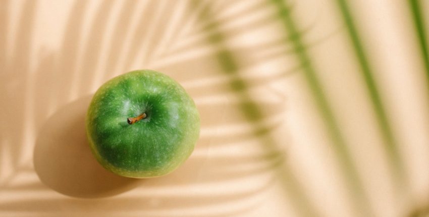 verdant green apple fruit with stem in shadow of palm trees
